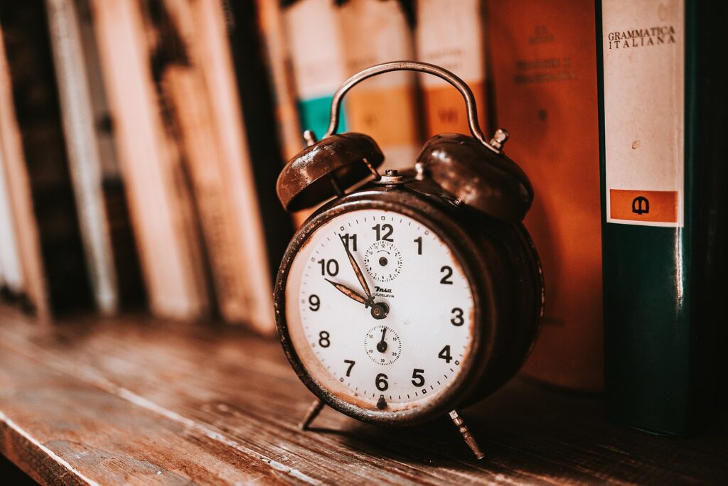 Vintage alarm clock on a wooden bookshelf, a reminder to set clocks back when daylight saving time ends