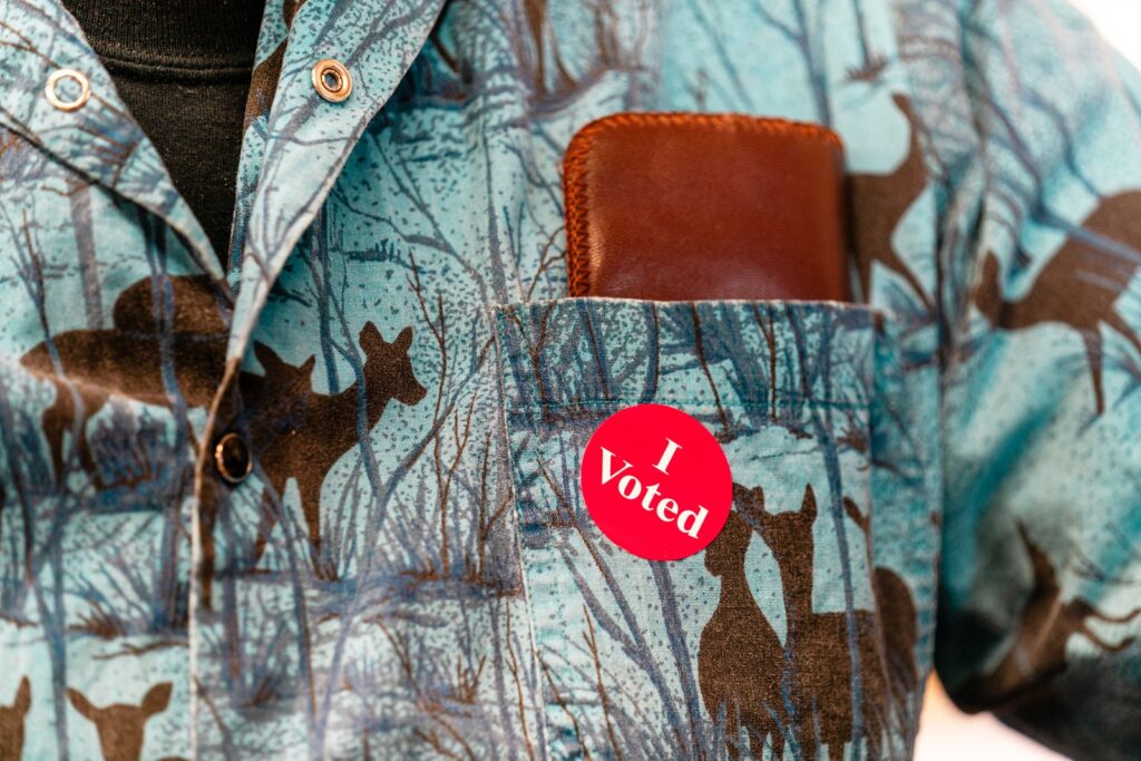 Red "I Voted" sticker on the pocket of a patterned blue shirt